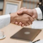 Close-up of two people shaking hands in an office, symbolizing agreement and partnership.