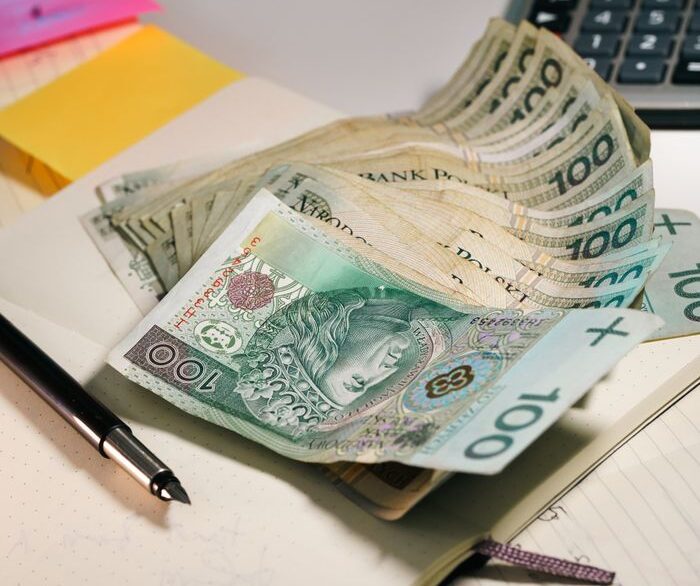 A stack of Polish Zloty banknotes on an office table with a calculator and notebook.
